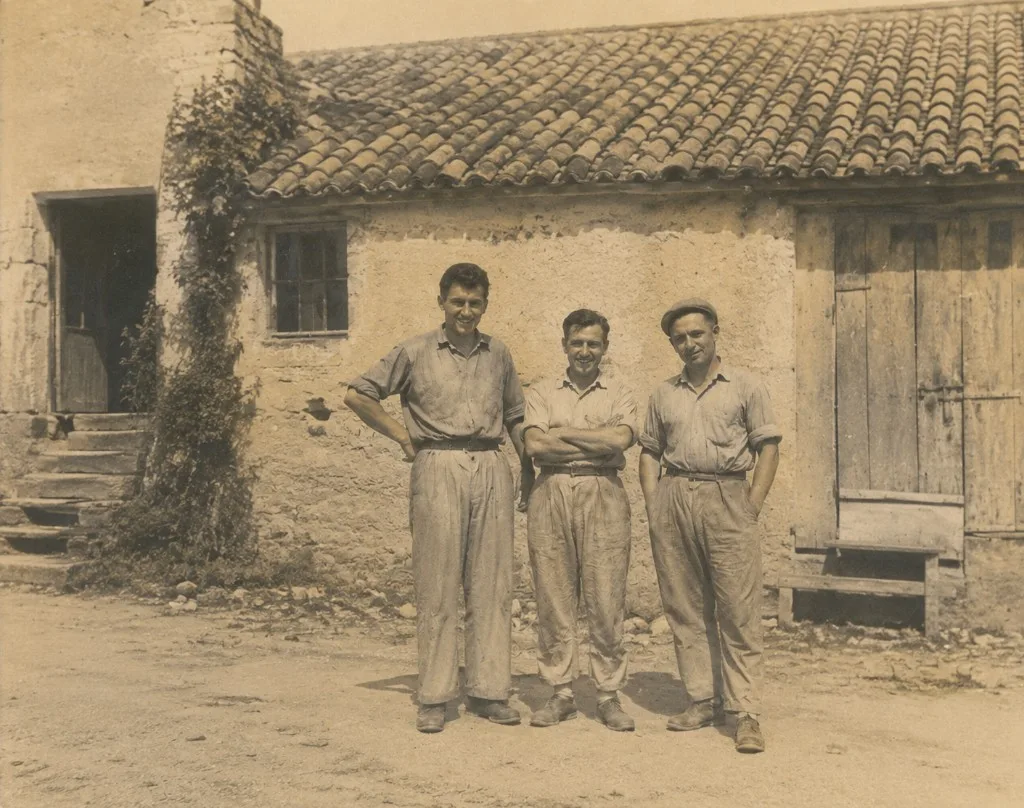 Vintage photograph of three workers standing outside a rustic stone farmhouse